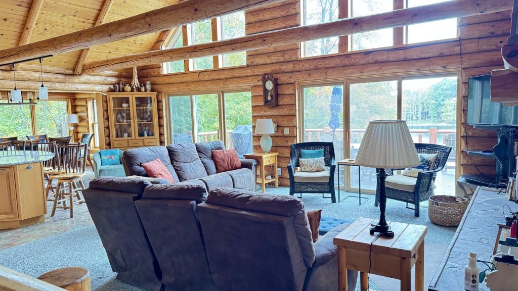 Great room with a log cathedral ceiling, tall windows, sofas and armchairs