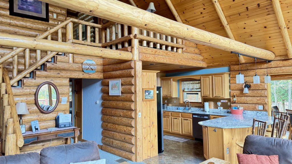 Living room with a log staircase up to the loft and the kitchen in the background