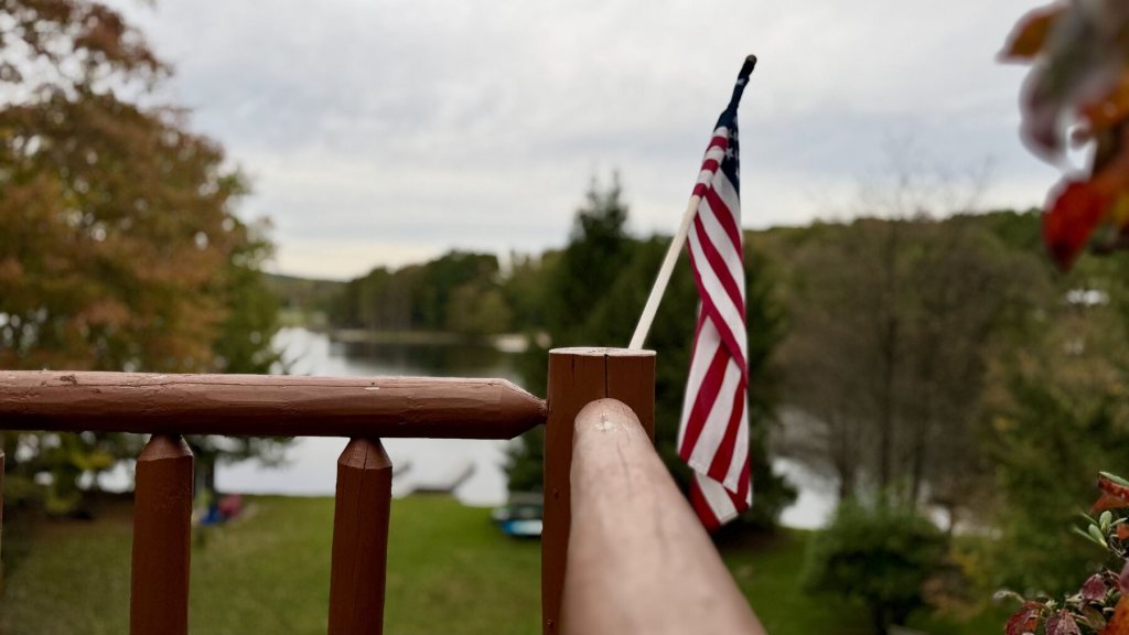 American flag on the deck railing with the lake and fall trees behind