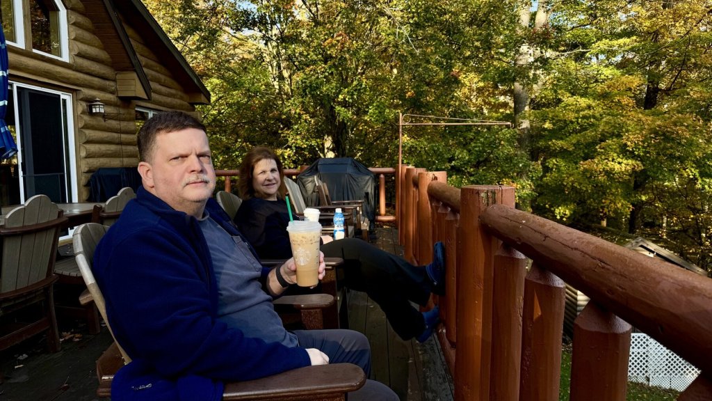 Corey and Katy relaxing with coffee on the cabin deck surrounded by fall trees