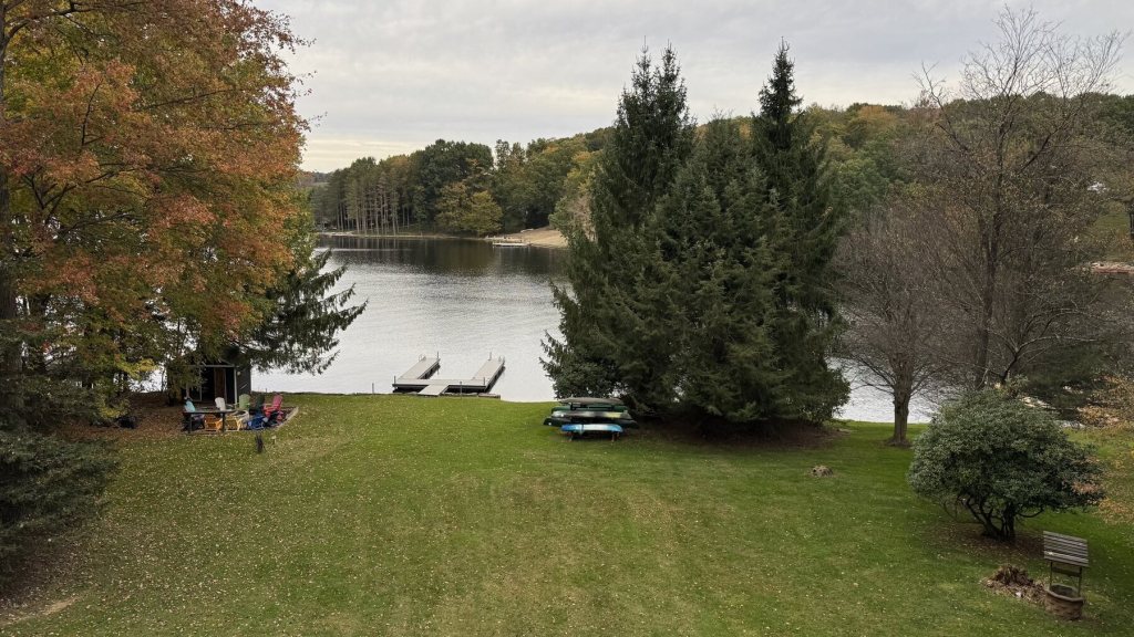 Green lawn sloping down to boat docks on the lake, with pines and fall trees