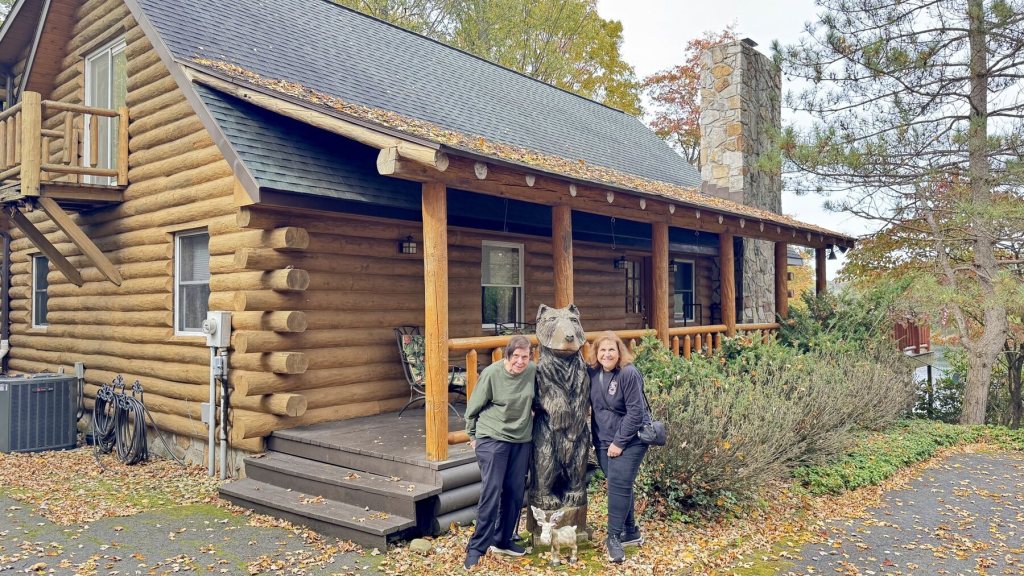 Katy and Ollie standing next to the carved wooden bear in front of the log cabin