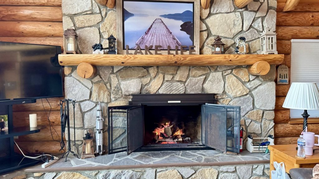 Wood fire burning in the stone fireplace of a log cabin at Treasure Lake, with a Lake Life picture above the mantel