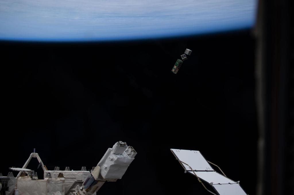 Three small CubeSat satellites being released into orbit from a deployer on the outside of the International Space Station's Kibo module