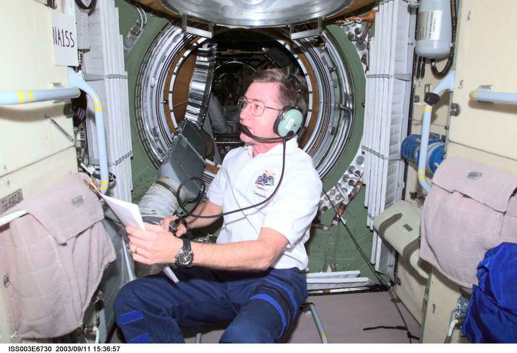 Astronaut Frank Culbertson holding a microphone while using a ham radio inside the Zarya module of the International Space Station.