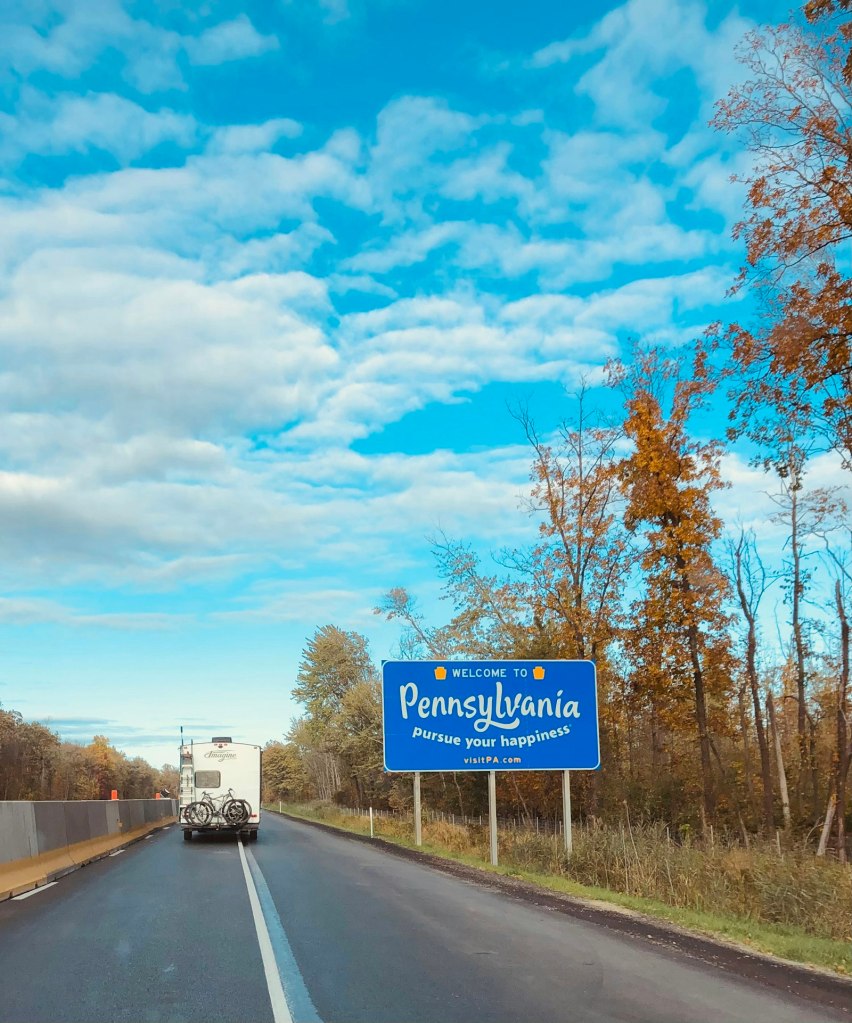 Blue and white road sign beside autumn trees