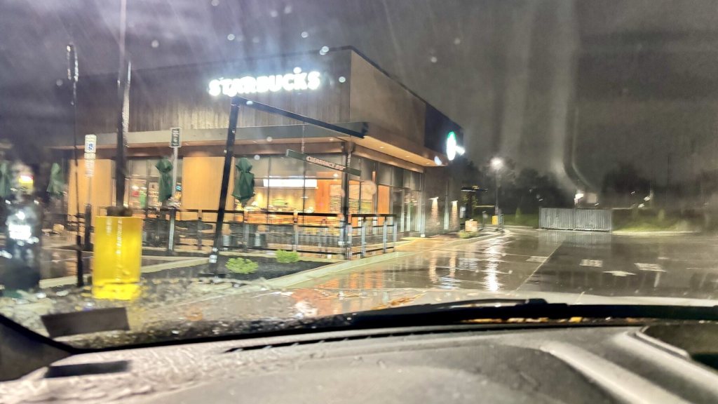 Lit Starbucks sign seen through a rain-covered windshield on a dark, wet morning in DuBois, PA